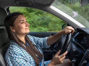 Mujer conduciendo un coche por una carretera rodeada de vegetación, manteniendo una conducción tranquila y eficiente para ahorrar gasolina.